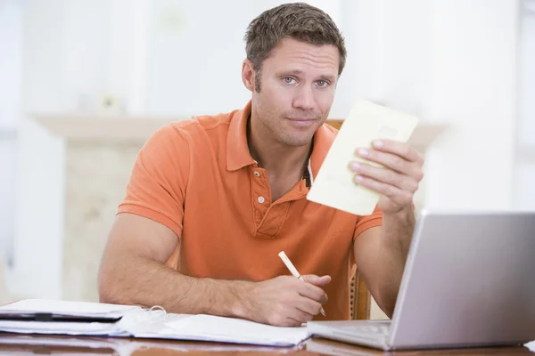 Man in dining room with laptop holding paperwork — Stock Photo, Image