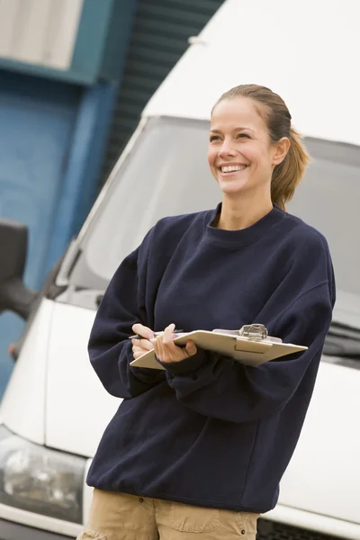 Deliveryperson standing with van writing in clipboard smiling — Stock Photo, Image