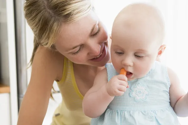 Mãe e bebê na cozinha comendo cenoura — Fotografia de Stock