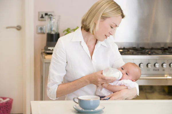 Mother feeding baby in kitchen with coffee — Stock Photo, Image