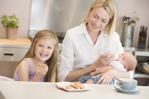 Mother feeding baby in kitchen with daughter eating cookies and — Stock Photo, Image