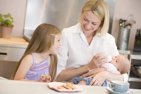 Mother feeding baby in kitchen with daughter eating cookies and — Stock Photo, Image