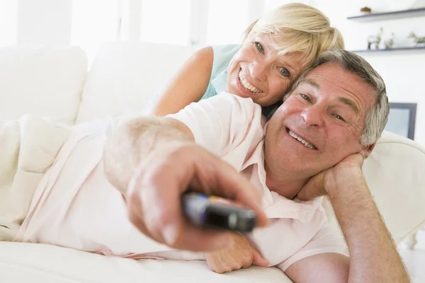 Par i vardagsrummet med hjälp av fjärrkontrollen leende — Stockfoto