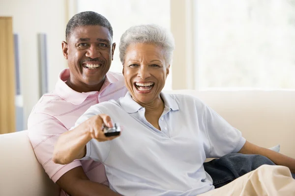 Casal na sala de estar usando controle remoto sorrindo — Fotografia de Stock