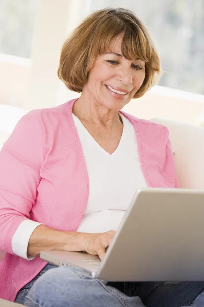 Γυναίκα στο σαλόνι με φορητό υπολογιστή χαμογελώντας — Φωτογραφία Αρχείου