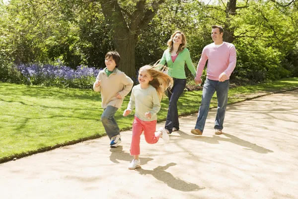 Familia corriendo en el camino tomados de la mano sonriendo — Foto de Stock