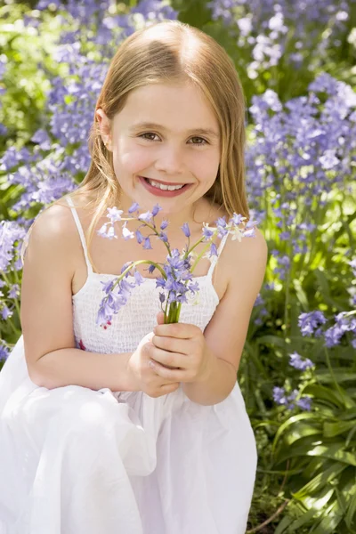 Young girl outdoors holding flowers smiling — Stock Photo, Image