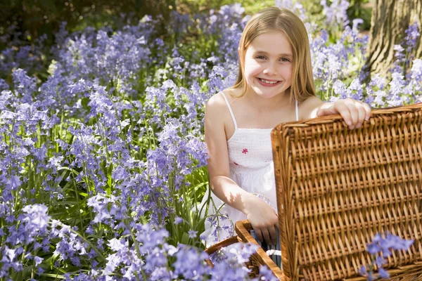 Young girl sitting outdoors with picnic basket smiling — Stock Photo, Image