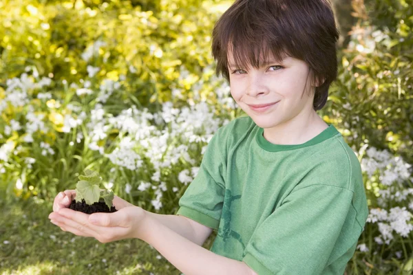 Joven chico al aire libre sosteniendo la planta sonriendo — Foto de Stock