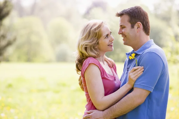 Paar umarmt sich im Freien und hält Blumen lächelnd in den Händen — Stockfoto