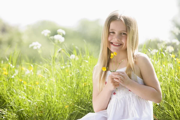 Jong meisje zitten buiten bedrijf bloem glimlachen — Stockfoto