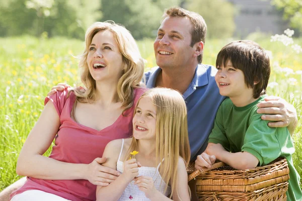 Familjen sitter utomhus med picknick korg leende — Stockfoto
