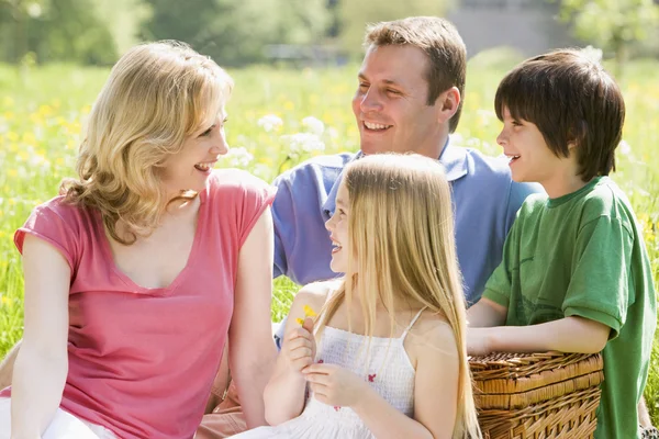 Familjen sitter utomhus med picknick korg leende — Stockfoto