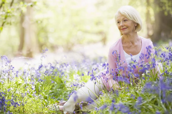 Mujer sentada al aire libre con flores sonriendo — Foto de Stock