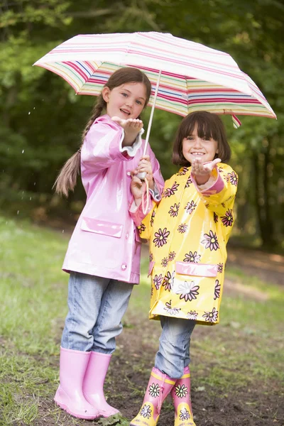 Two sisters outdoors in rain with umbrella smiling — Stock Photo, Image