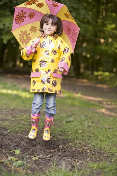 Young girl outdoors with umbrella jumping and smiling — Stock Photo, Image