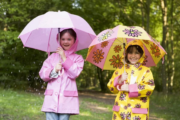 Two sisters outdoors in rain with umbrellas smiling — Stock Photo, Image