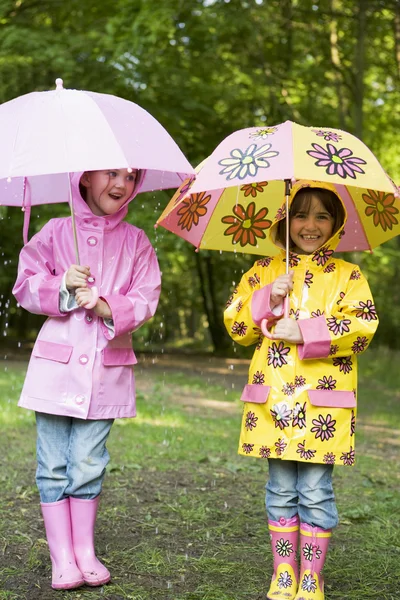 Twee zusters buiten in de regen met paraplu's glimlachen — Stockfoto