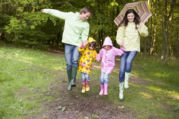 Family outdoors skipping with umbrella smiling — Stock Photo, Image