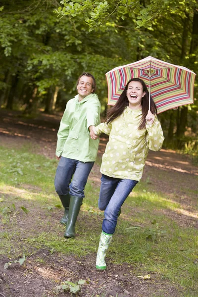 Couple outdoors running with umbrella smiling — Stock Photo, Image