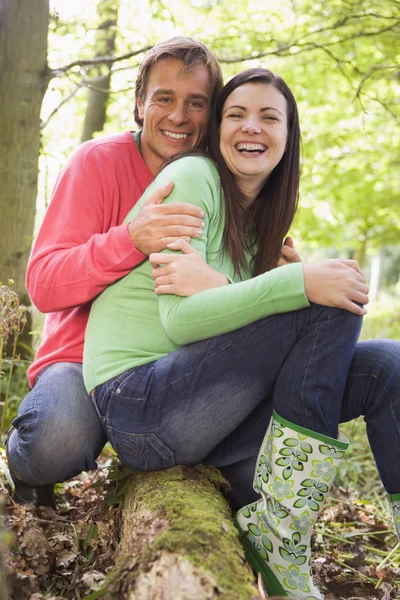 Couple à l'extérieur dans les bois assis sur rondins souriant — Photo