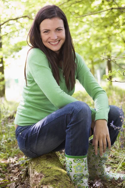 Woman outdoors in woods sitting on log smiling — Stock Photo, Image