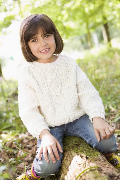 Young girl outdoors in woods sitting on log smiling — Stock Photo, Image