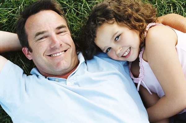 Vader en dochter liggen buiten lachende — Stockfoto