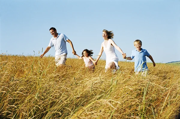 Семья бежит на свежем воздухе, держа руки улыбаясь — стоковое фото