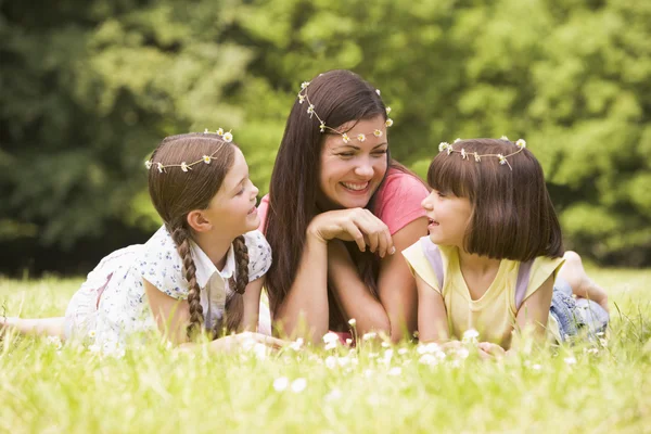 Mother and daughters lying outdoors with flowers smiling — Stock Photo, Image