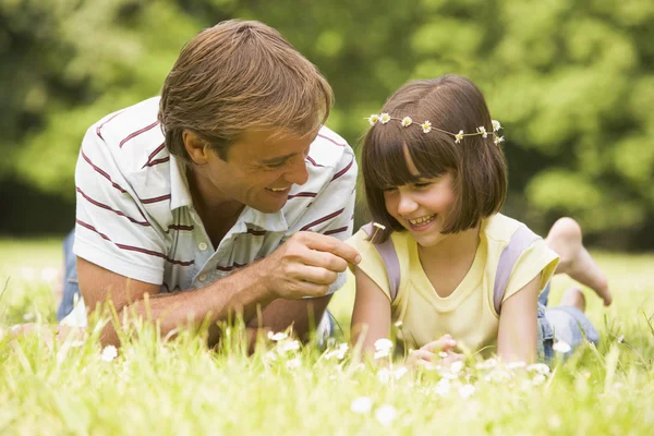 Father and daughter lying outdoors with flowers smiling — Stok fotoğraf