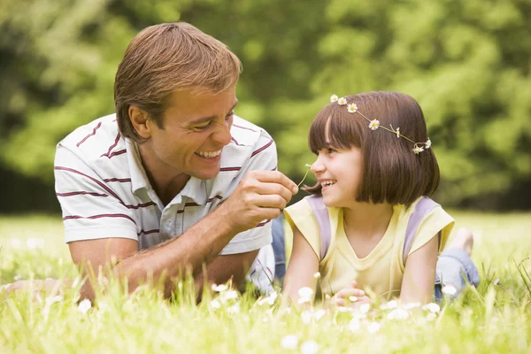 Father and daughter lying outdoors with flowers smiling — Stok fotoğraf