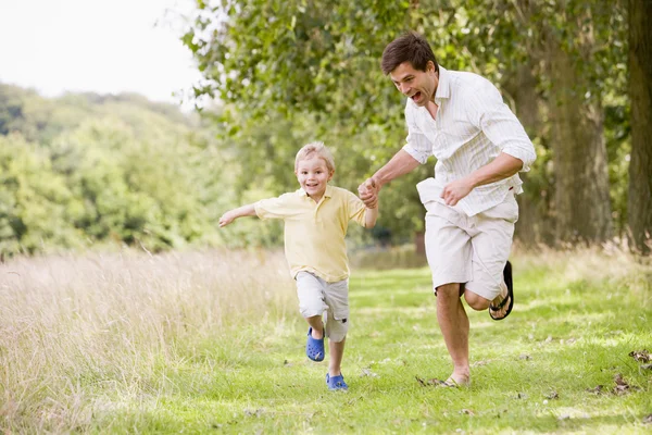 Отец и сын бегут по тропинке, держась за руки и улыбаясь — стоковое фото