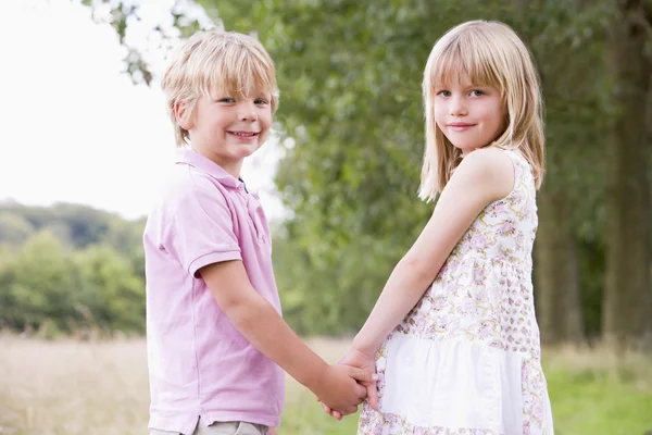 Duas crianças pequenas de pé ao ar livre de mãos dadas sorrindo — Fotografia de Stock