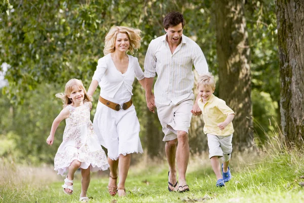 Familia corriendo en el camino tomados de la mano sonriendo —  Fotos de Stock