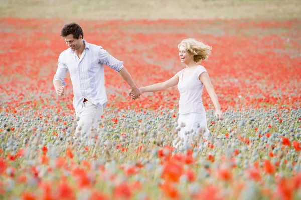 笑みを浮かべて手を繋いでケシ畑で歩くカップル — ストック写真