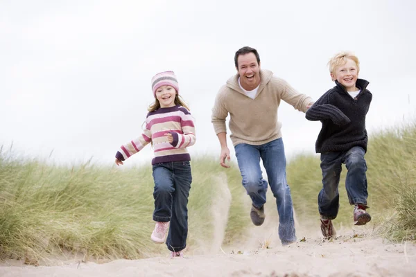 Padre y dos niños pequeños corriendo por la playa sonriendo —  Fotos de Stock