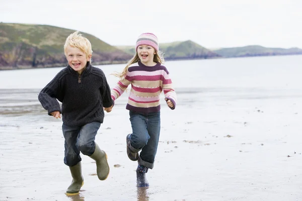 Dos niños pequeños corriendo por la playa tomados de la mano sonriendo —  Fotos de Stock