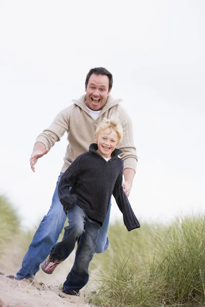Pai e filho correndo na praia sorrindo — Fotografia de Stock