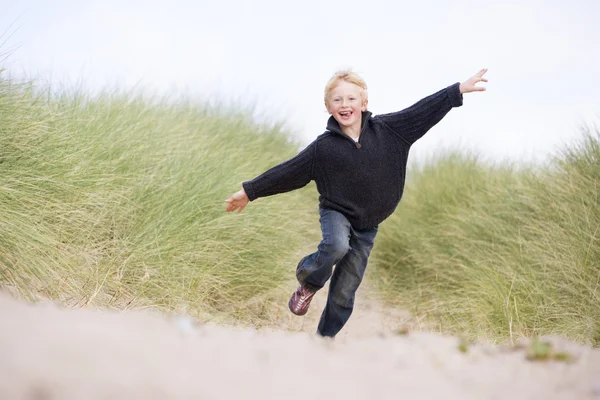 Ung pojke körs på stranden leende — Stockfoto