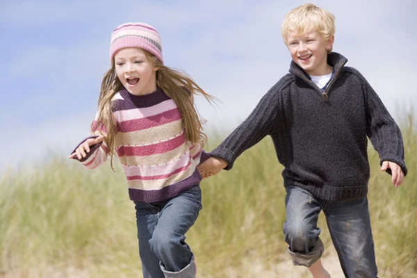 Двое маленьких детей бегут по пляжу, держась за руки и улыбаясь — стоковое фото