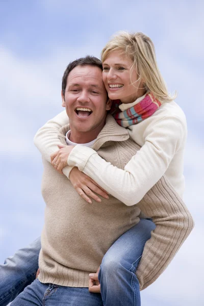 Mannen ger kvinnan piggyback rida utomhus leende — Stockfoto