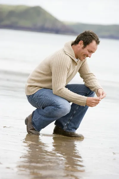 Homem agachado na praia sorrindo — Fotografia de Stock