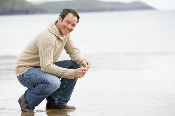 Homem agachado na praia — Fotografia de Stock