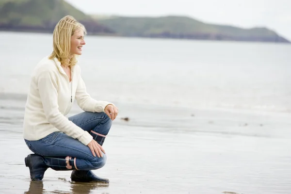 Женщина, присевшая на пляже, улыбаясь — стоковое фото