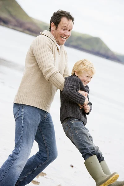 Отец держит сына на пляже улыбаясь — стоковое фото