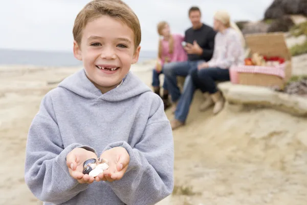 Rodzina na plaży z pikniku uśmiechający się skupić na chłopca z muszelek — Zdjęcie stockowe