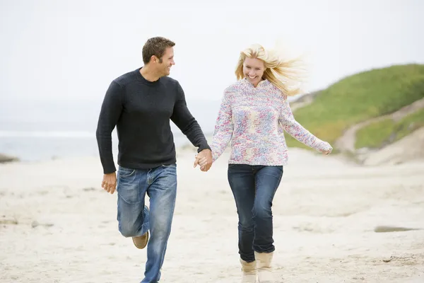 Pareja corriendo en la playa tomados de la mano sonriendo — Foto de Stock