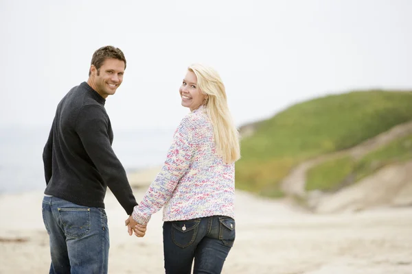 笑みを浮かべて手を繋いでいるビーチで歩くカップル — ストック写真