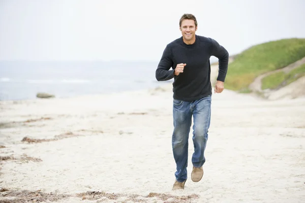 Мужчина бежит по пляжу улыбаясь — стоковое фото